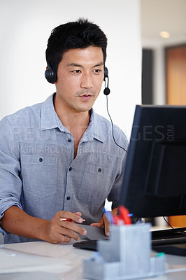 Buy stock photo Shot of an Asian man using a computer and talking on a headset