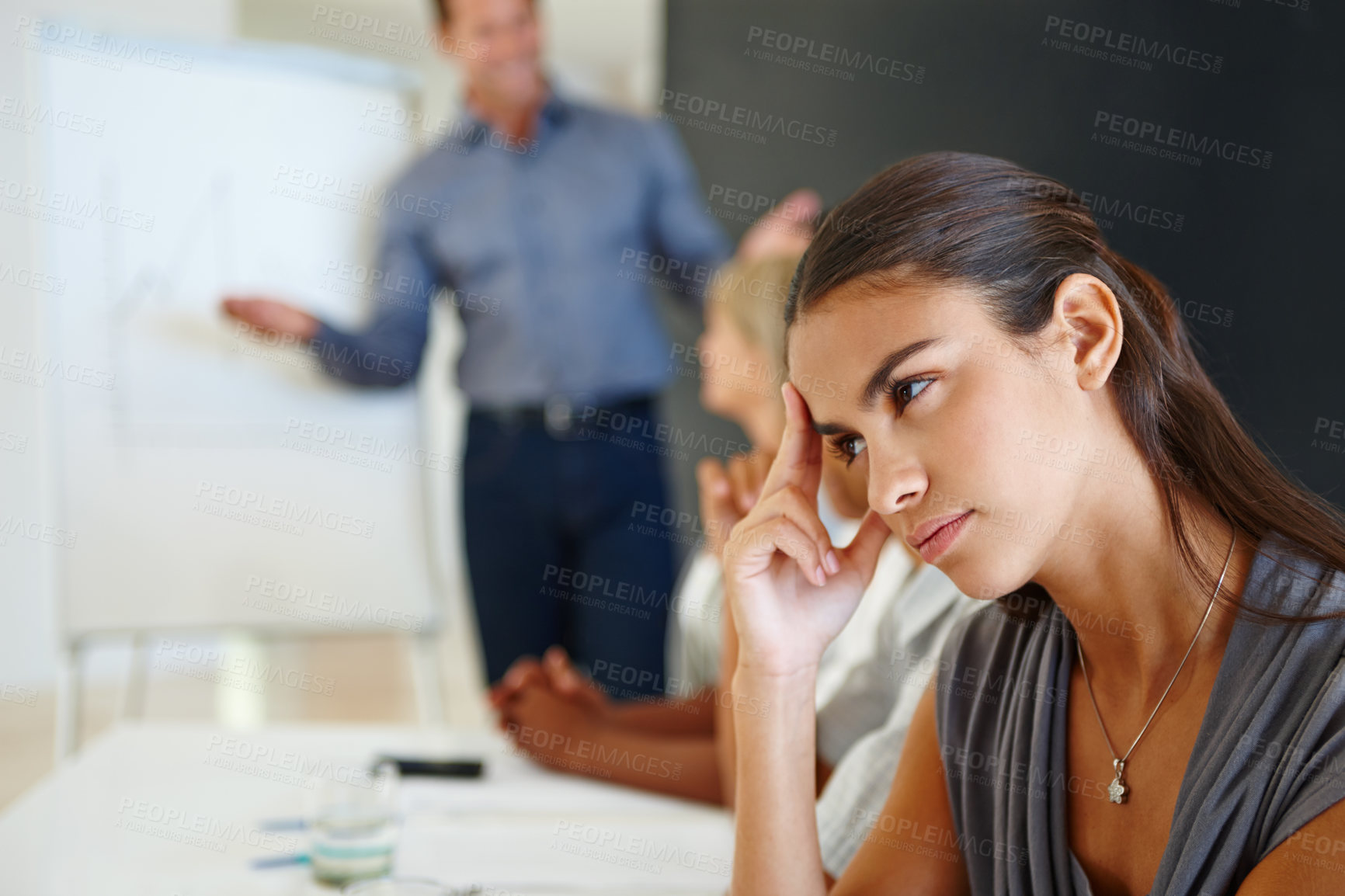 Buy stock photo Young businesswoman looking bored in a meeting her with hand on her temple