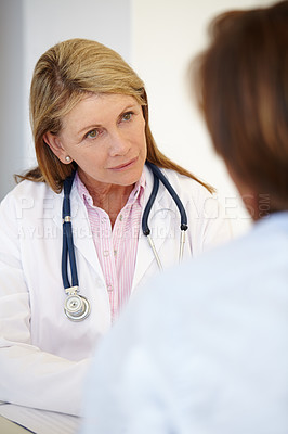 Buy stock photo A mature female doctor listening to a patient. Serious unsmiling woman in a lab coat and stethoscope inquiring about patients health. Senior healthcare professional giving support care during checkup