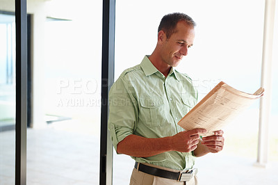 Buy stock photo Man, newspaper and morning reading in home, news articles and headlines for information and standing before work. Happy, smile male person and relaxed in apartment with newsletter for entertainment