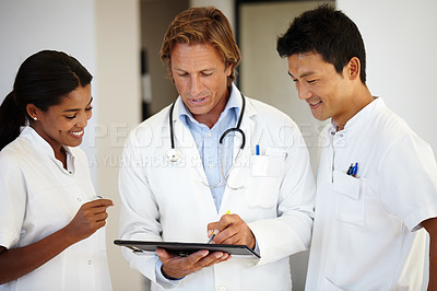 Buy stock photo Shot of three doctors looking at a digital tablet