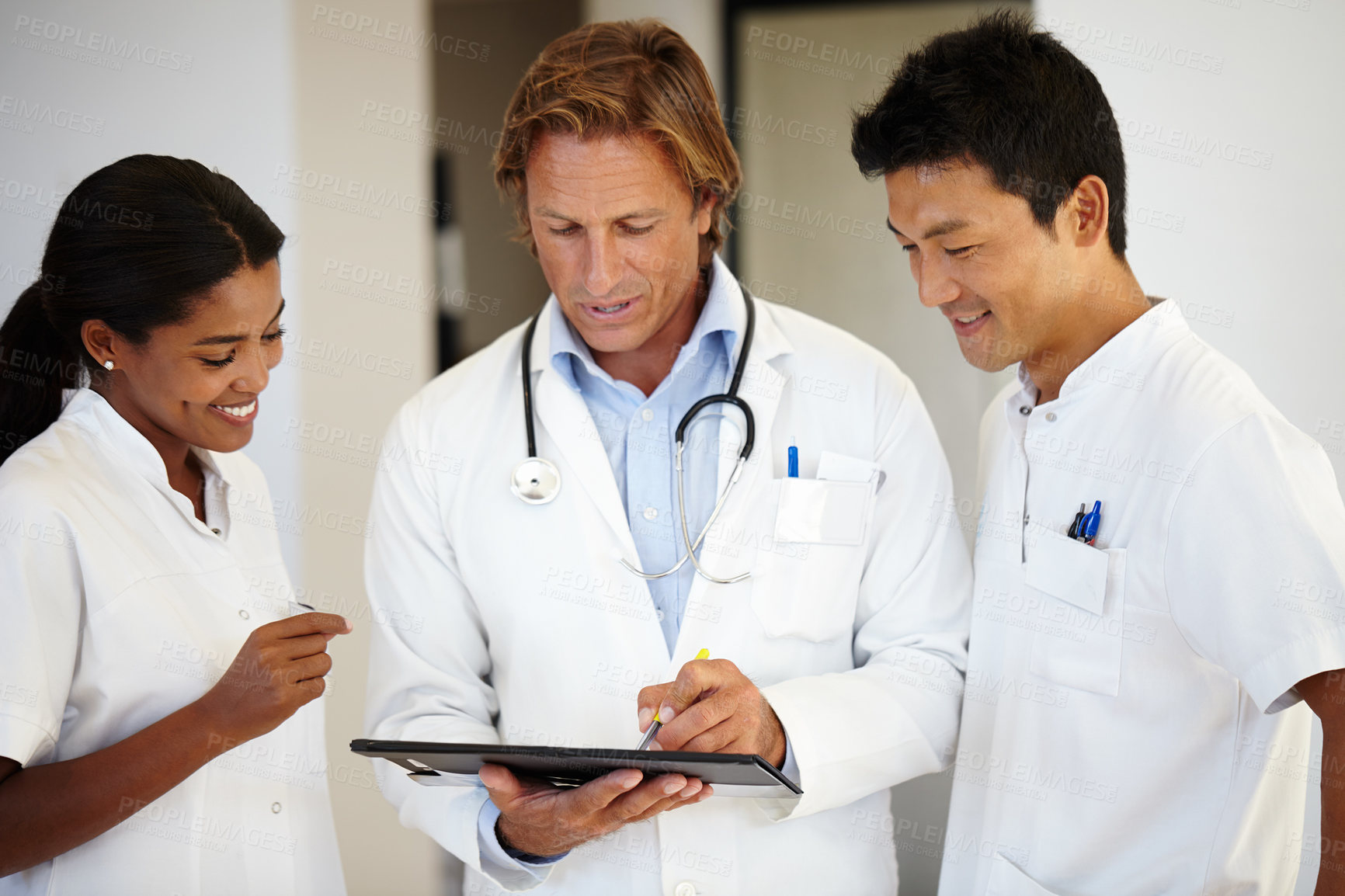 Buy stock photo Shot of three doctors looking at a digital tablet