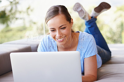 Buy stock photo Shot of a young woman relaxing on a couch while using a laptop