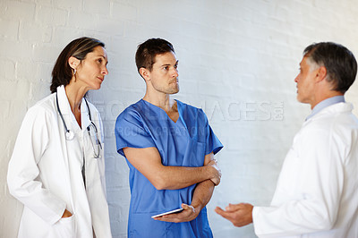 Buy stock photo A cropped shot of three doctors standing and having a serious conversation