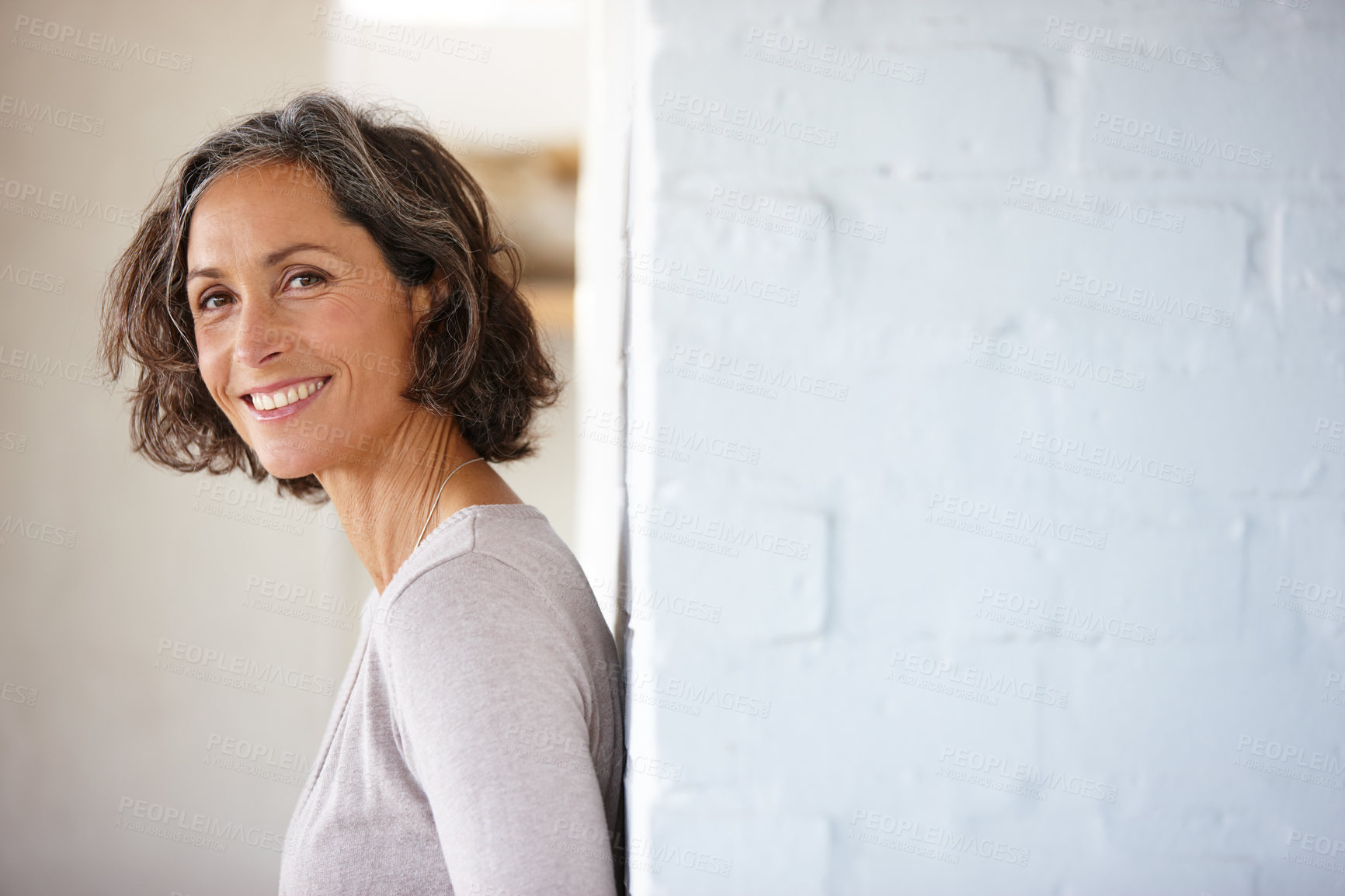 Buy stock photo Shot of an attractive mature woman leaning against a wall