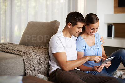 Buy stock photo An affectionate young couple using a tablet in their living room