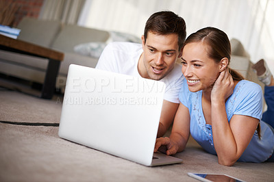 Buy stock photo A happy young couple lying on their living room floor with a laptop