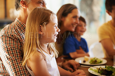 Buy stock photo Shot of a little girl sitting on her grandfather's lap at dinner with her family in the background