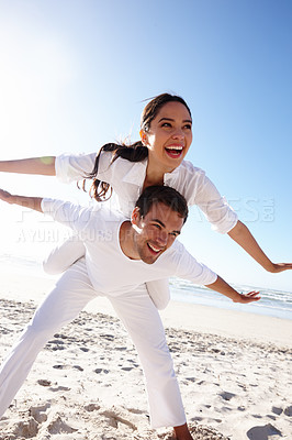 Buy stock photo Cropped shot of a young man giving his girlfriend a piggyback at the beach