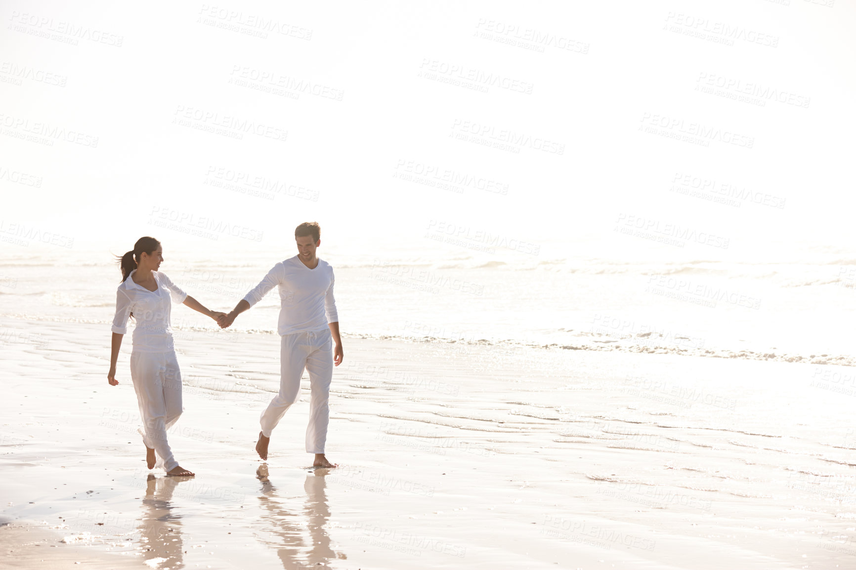 Buy stock photo Full length shot of an attractive young couple dressed in white walking along a beach