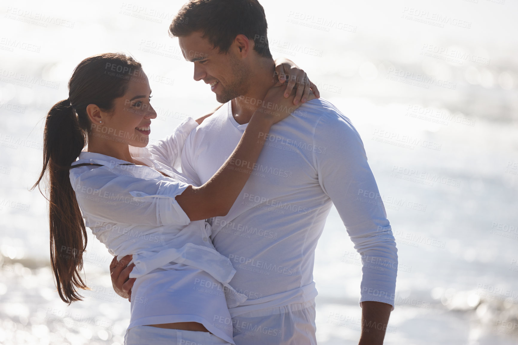 Buy stock photo Cropped shot of a young couple embracing at the beach