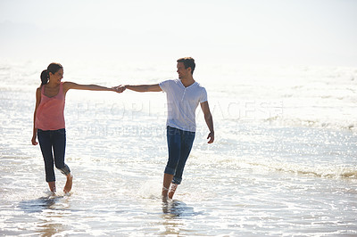 Buy stock photo Shot of a young couple holding hands while walking by the beach