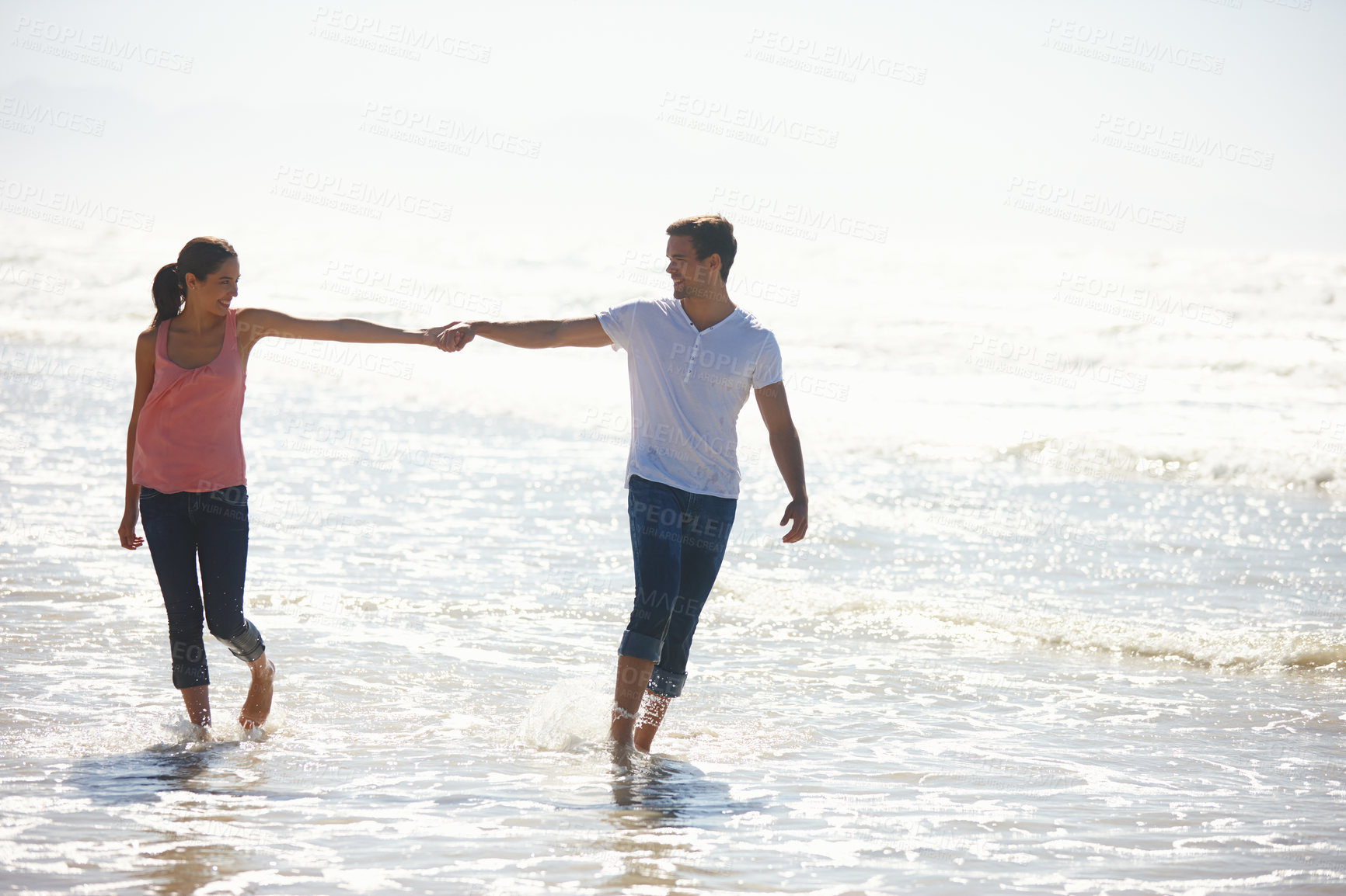 Buy stock photo Shot of a young couple holding hands while walking by the beach