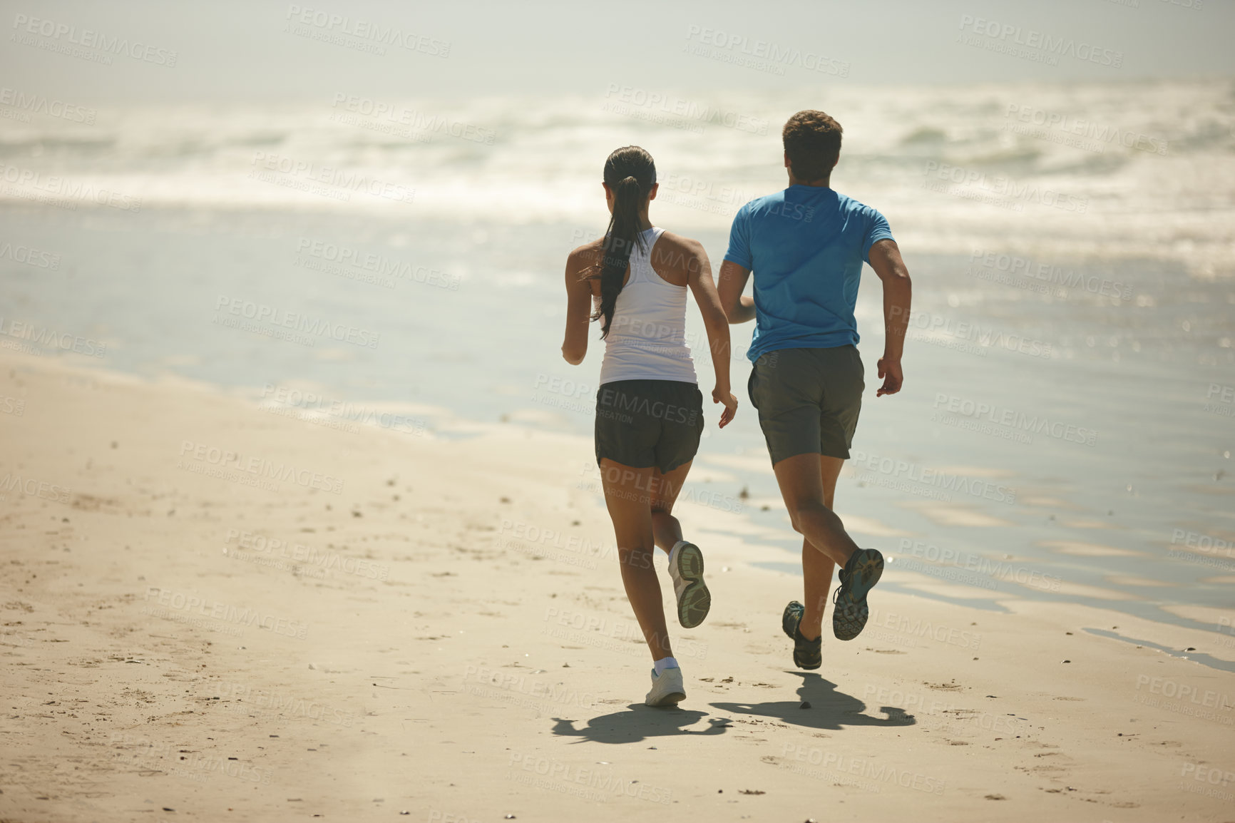 Buy stock photo Rearview shot of a young couple jogging together on the beach
