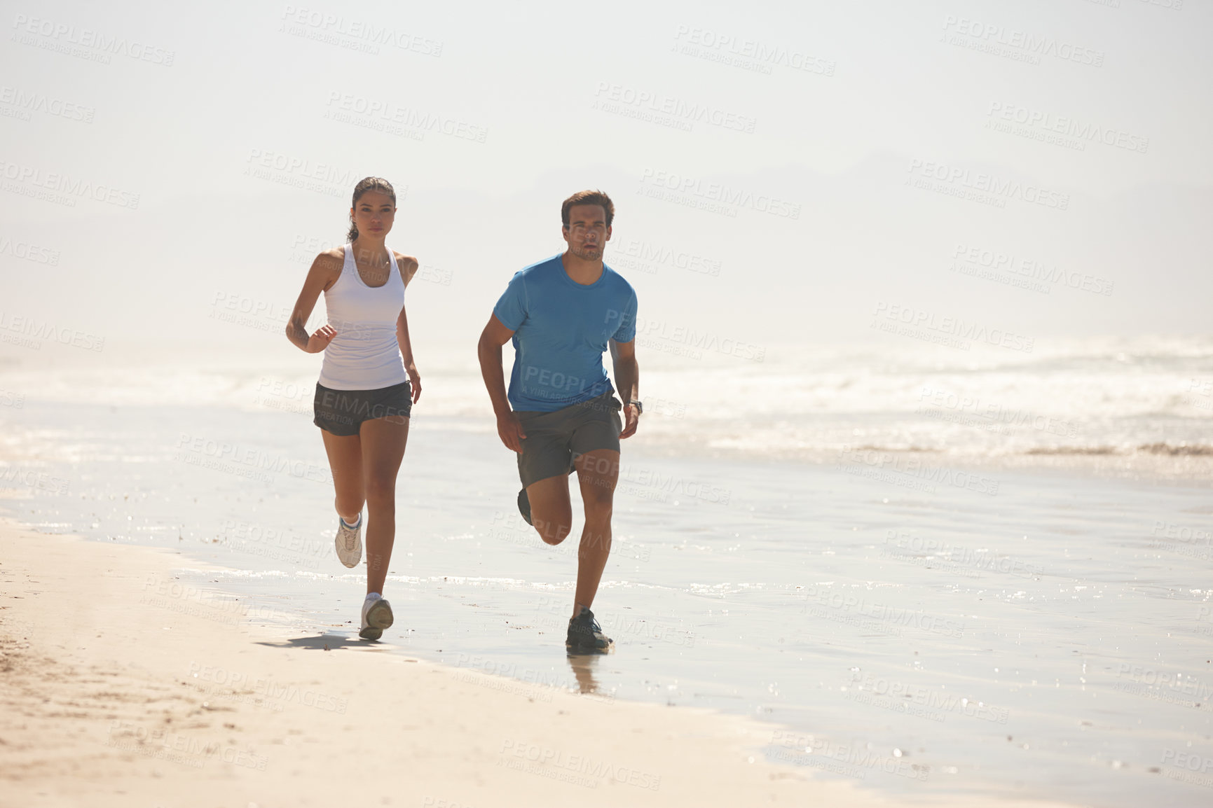 Buy stock photo Shot of a young couple jogging together on the beach