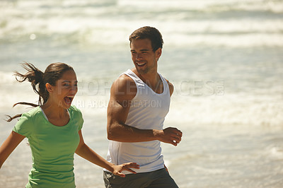 Buy stock photo Shot of a laughing young couple jogging together on the beach