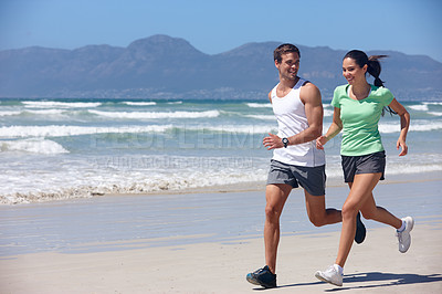 Buy stock photo Shot of a young couple jogging together on the beach