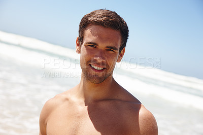 Buy stock photo Portrait of a confident hunk smiling while standing on the beach in summer. Carefree man suntanning while spending time by the sea. Cool dude enjoying seaside vacation and ready to swim in the ocean