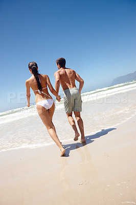 Buy stock photo Couple, rear view and holding hands by beach with travel for bonding, summer vacation and anniversary getaway. Man, woman and love by ocean with swimwear for walking, healthy relationship or blue sky