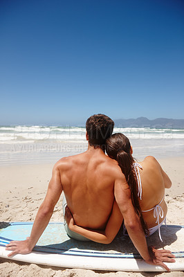 Buy stock photo Rearview shot of a young couple sitting on a surfboard while looking at the ocean