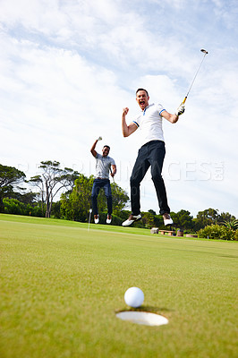 Buy stock photo Low angle shot of a golf ball approaching the hole while two golfers look on