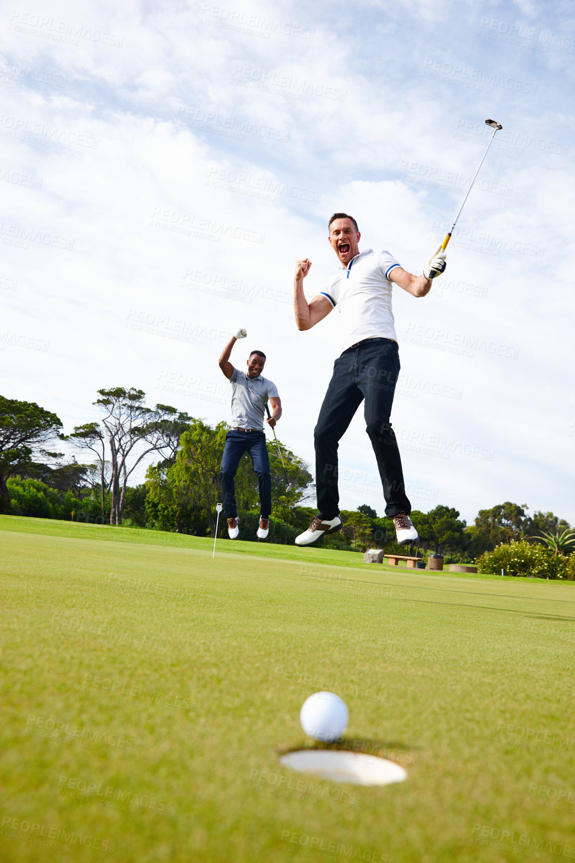 Buy stock photo Low angle shot of a golf ball approaching the hole while two golfers look on