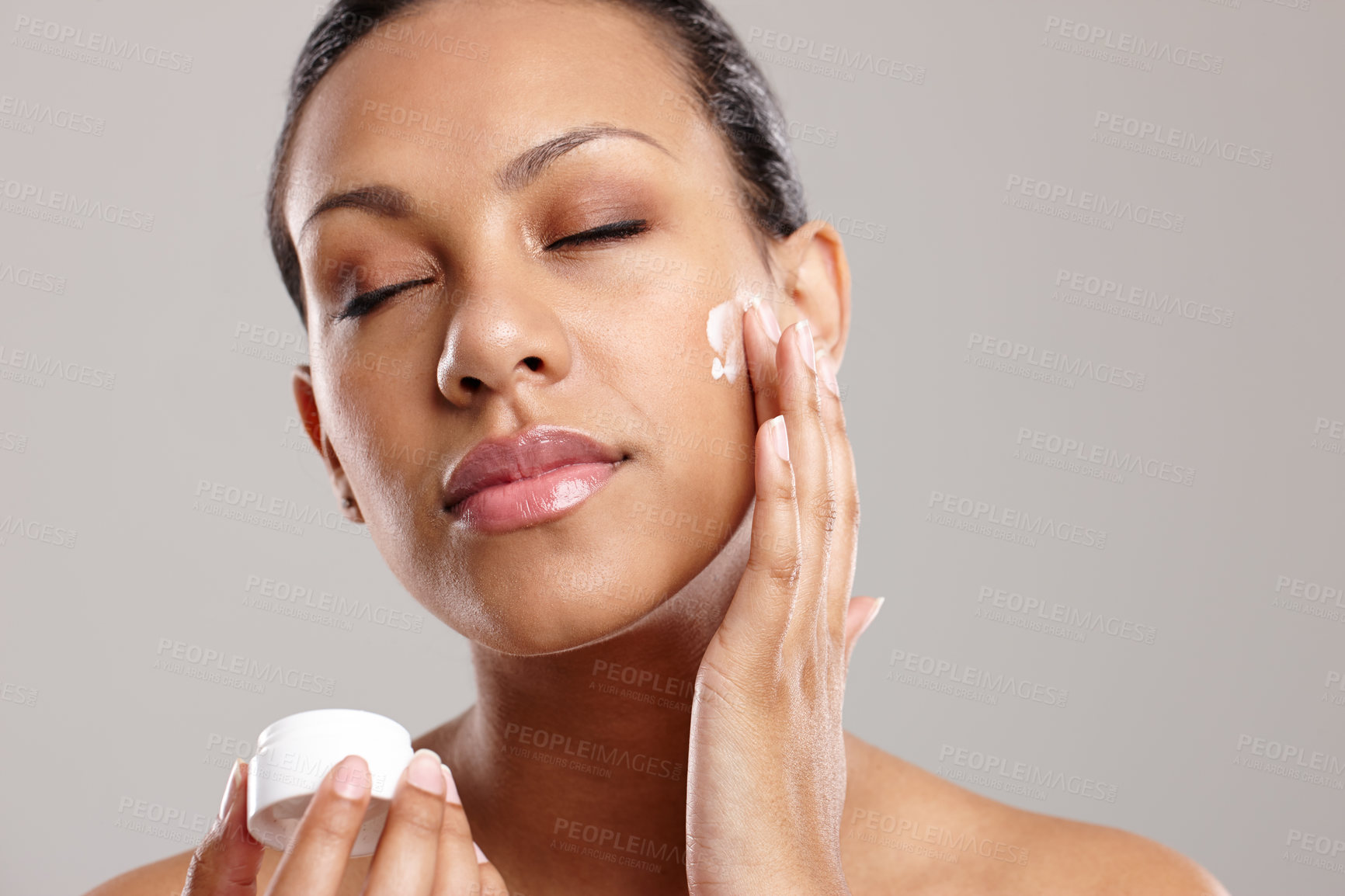 Buy stock photo Cropped shot of a beautiful young woman applying face cream while standing in a studio