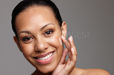 Buy stock photo Cropped shot of a beautiful young woman applying face cream while standing in a studio