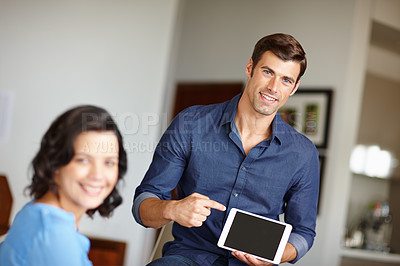 Buy stock photo A handsome man pointing at his digital tablet while sitting at home with his wife