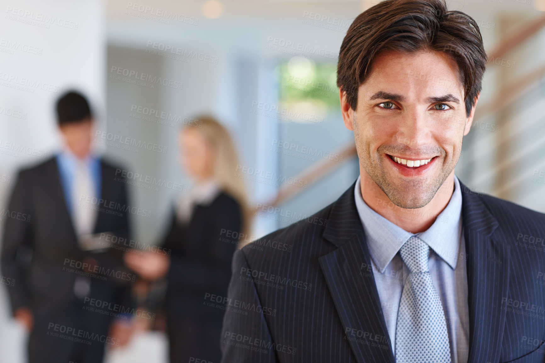 Buy stock photo Portrait of a businessman standing indoors with two colleagues in the background