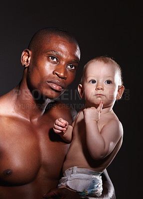 Buy stock photo Concept shot of a man holding a little boy in his arms against a black background
