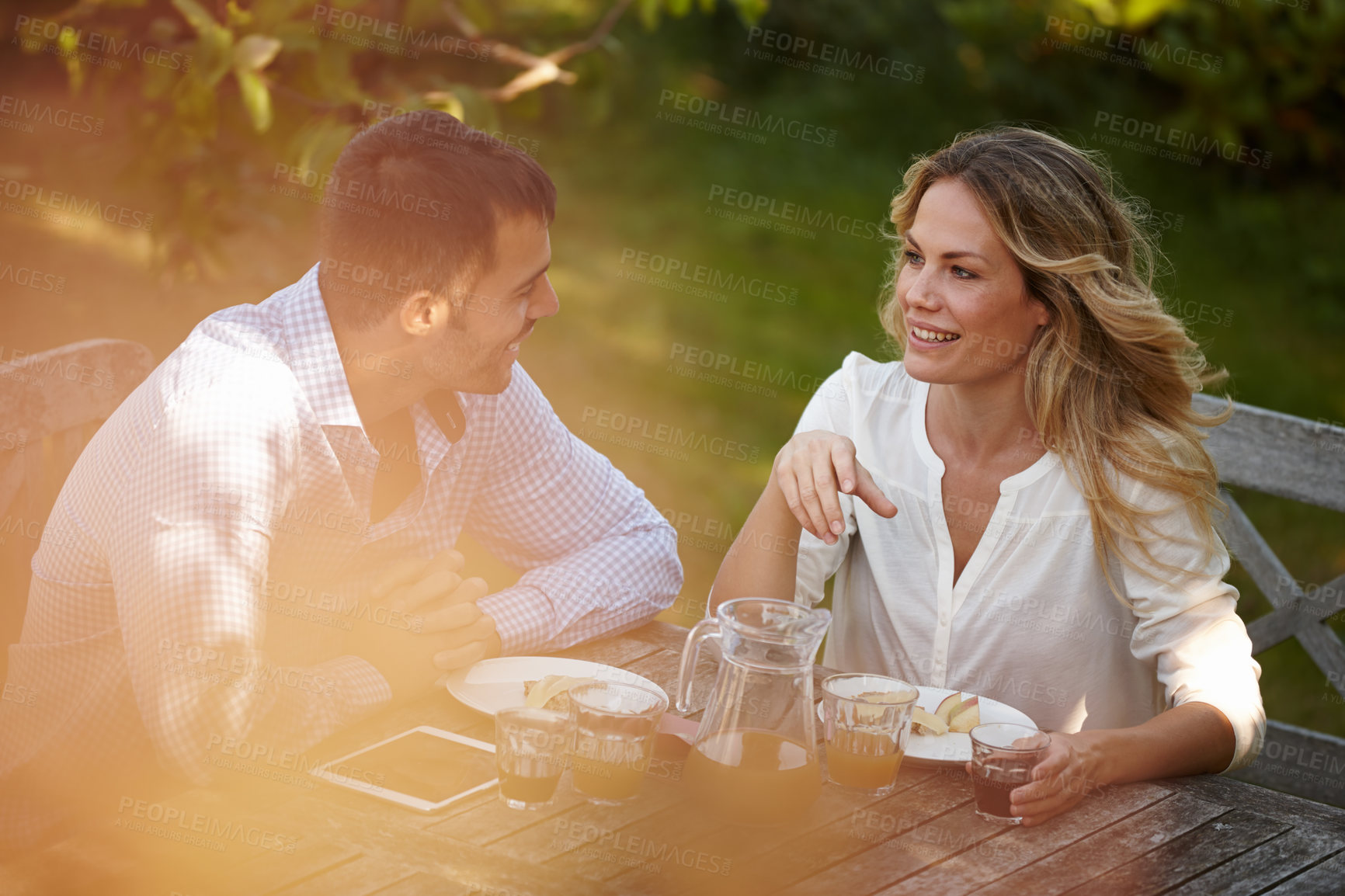 Buy stock photo Couple, outdoors or dinner with tablet and smile at sunset, conversation for relationship or marriage. Female, male person or outside at table for meal with technology, healthy communication or juice