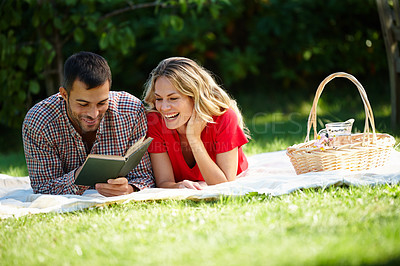 Buy stock photo Shot of a happy young couple reading a book while having a picnic in a park