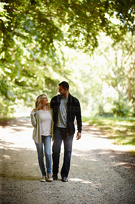 Buy stock photo Full length shot of a young couple walking arm in arm in a park