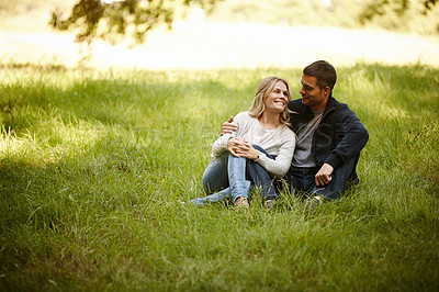 Buy stock photo Shot of a loving young couple sitting on the grass in a park