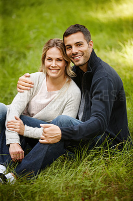 Buy stock photo Portrait of a loving young couple sitting on the grass in a park