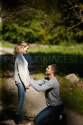 Buy stock photo Shot of a man kneeling and touching his wife's stomach while enjoying a day in the park