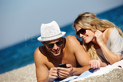 Buy stock photo Couple, sunglasses and relax on beach towel, phone and social media at summer or lying by water. People, app and tropical ocean for bonding on weekend, outdoor nature and love for marriage or typing