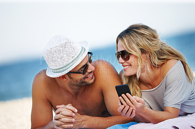 Buy stock photo Couple, sunglasses and lying on beach towel, phone and social media at beach or calm by water. People, app and tropical ocean for bonding on weekend, outdoor nature and love for marriage or typing 
