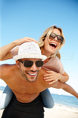 Buy stock photo Shot of a smiling young man giving his laughing girlfriend a piggyback on a sunny beach