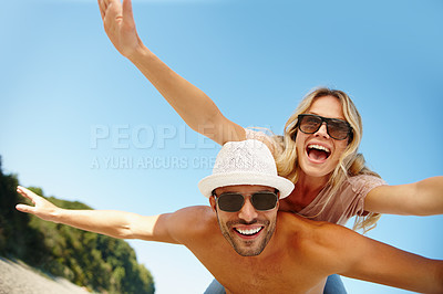 Buy stock photo Couple, sunglasses and piggyback on vacation, fun and peace at beach or game by blue sky. People, happy and tropical island for bonding on weekend, outdoor nature and love for marriage or romance