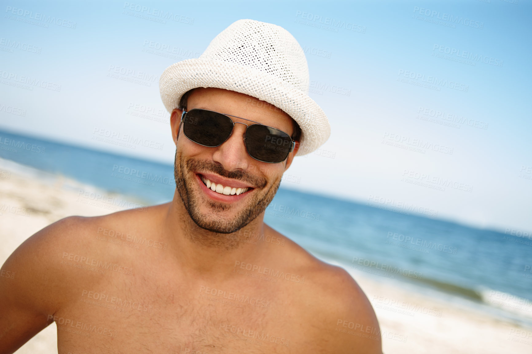 Buy stock photo Portrait, happy man and sunglasses at Brazilian beach with blue sky for summer vacation, topless and hat. Male tourist, smile and island with water in outdoor for traveling, sunny and ocean holiday 