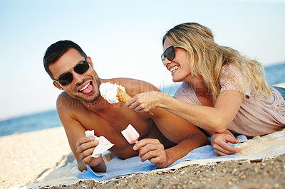 Buy stock photo Shot of a happy young couple eating ice cream while lying on a sunny beach