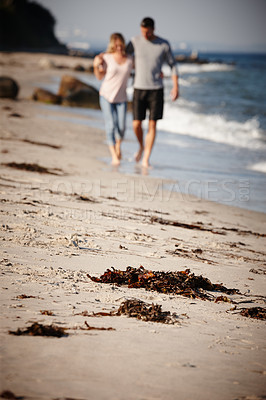 Buy stock photo Full length shot of a young couple walking arm in arm along a sandy beach