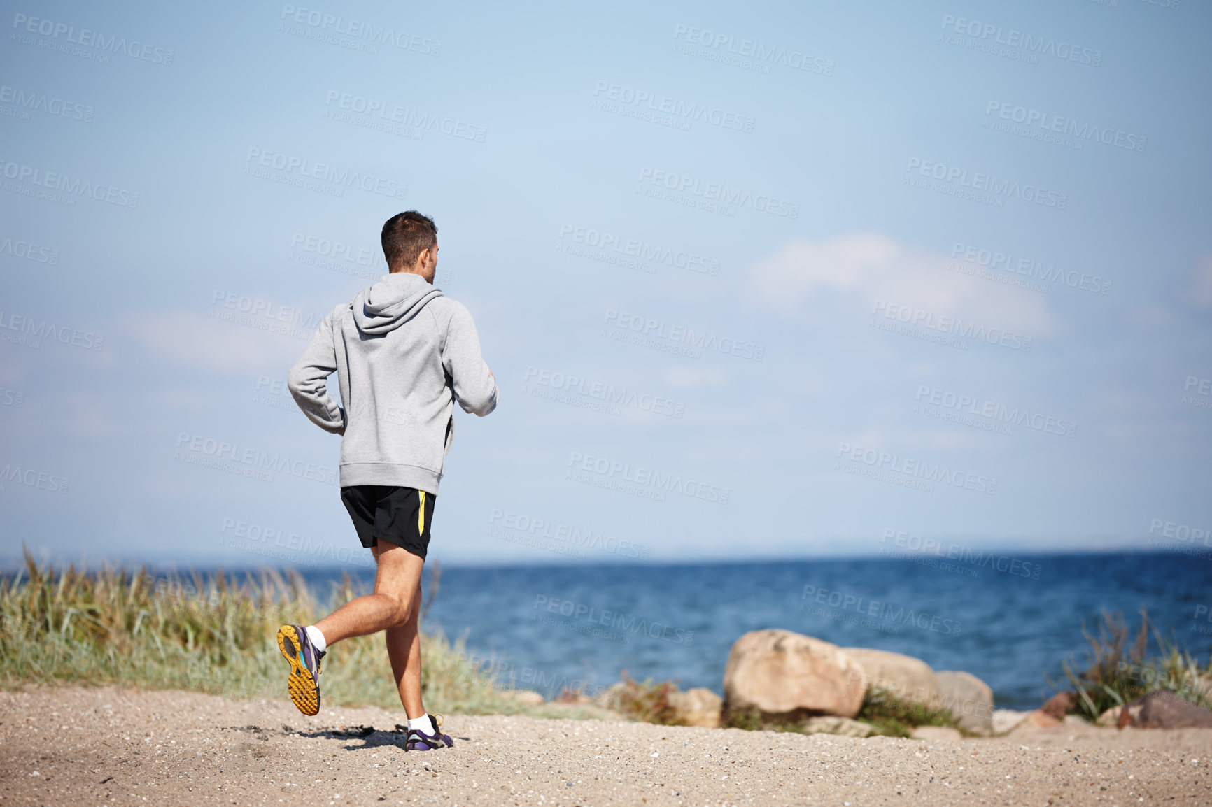 Buy stock photo Rearview shot of a young man running on the beach