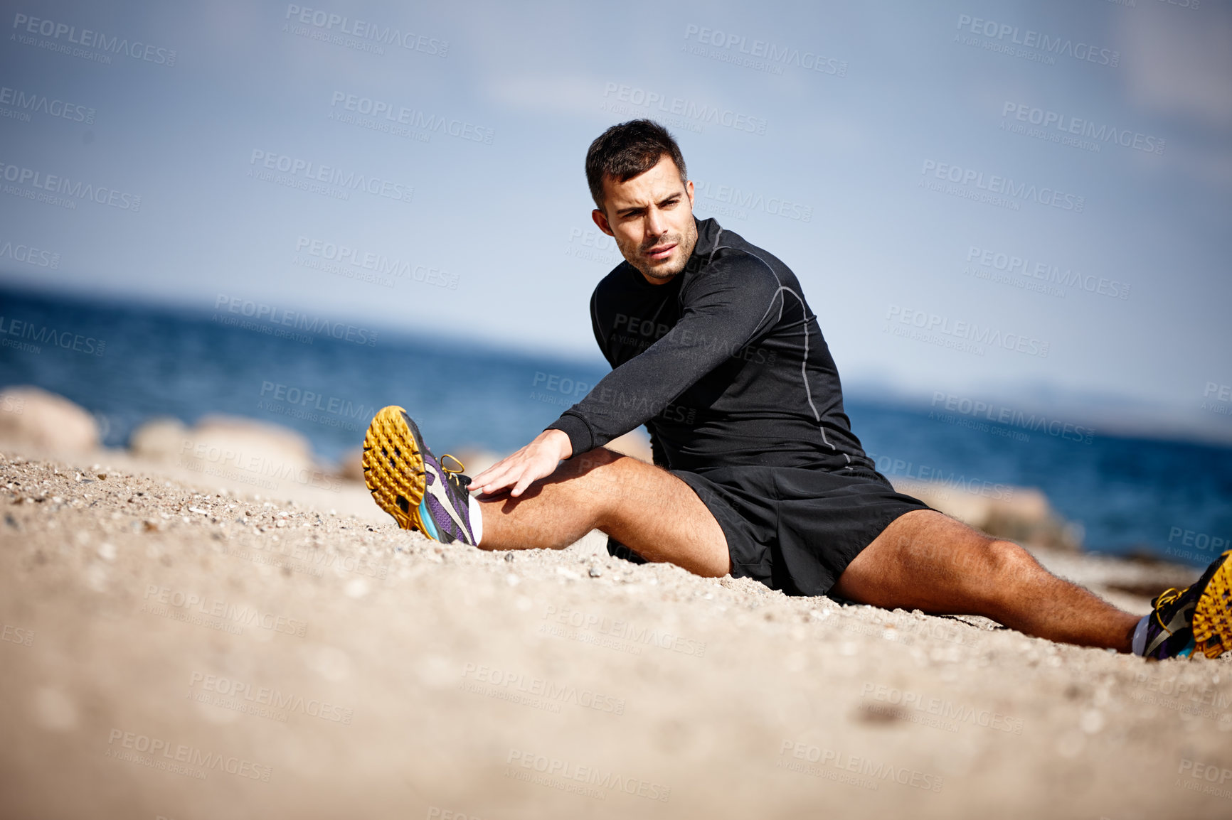 Buy stock photo Man, stretching and blue sky at beach for exercise with fitness motivation, sand and sports. Male person, training and nature by ocean with workout for wellness, strong body and health activity