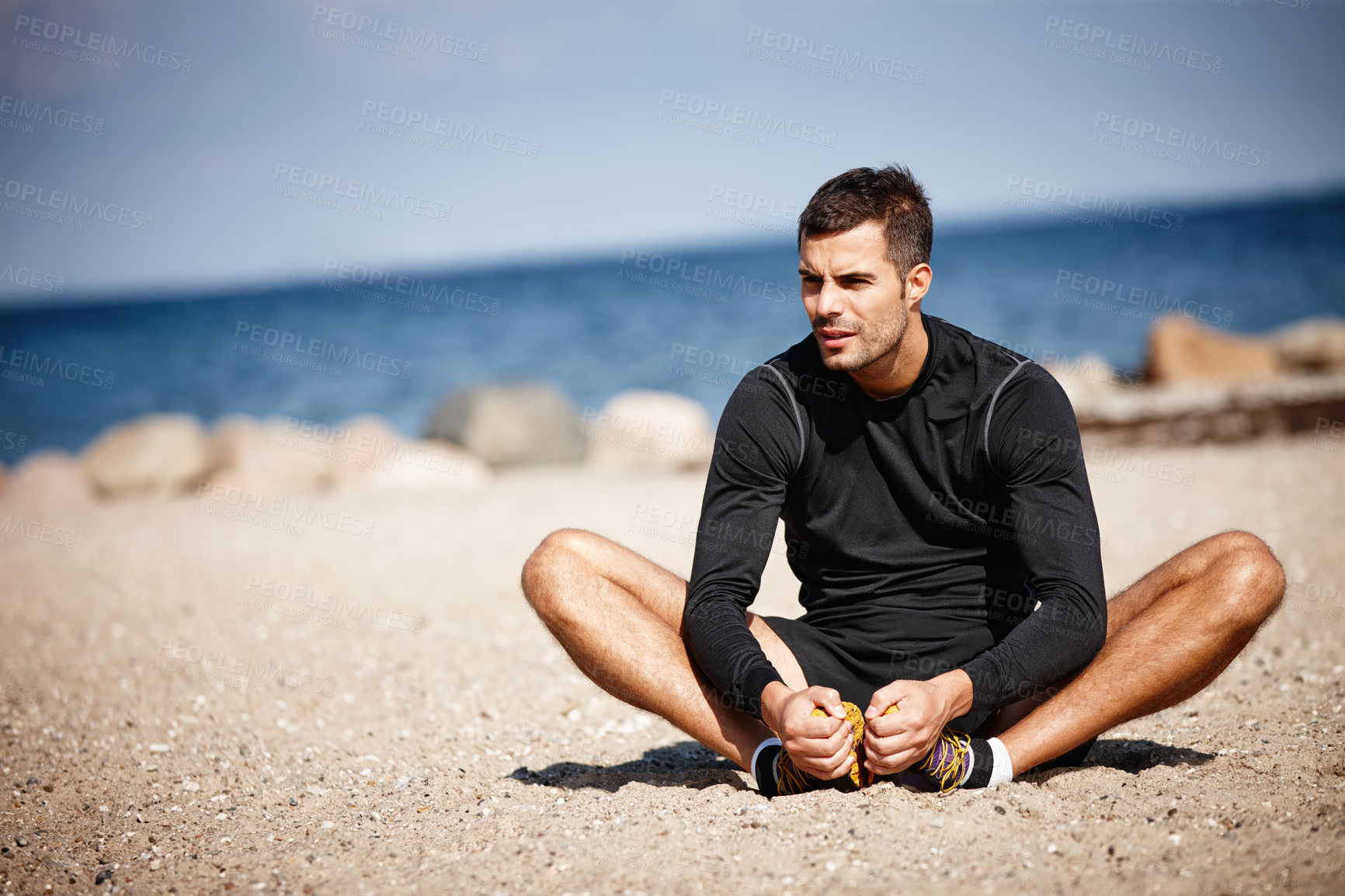 Buy stock photo Man, exercise and sports at ocean for stretching with fitness motivation, sand and blue sky. Male person, training and nature by beach with workout for wellness, strong body and health activity