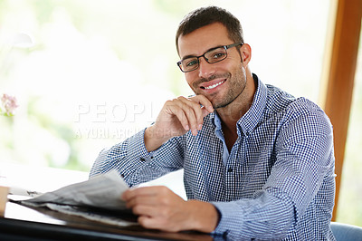 Buy stock photo Portrait of a smiling young man reading the newspaper