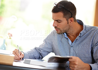 Buy stock photo Young man or studying with books or pen for job, busy learning or writing with focus at desk. Male student or determination for professional development in home, reading glasses for notes with paper