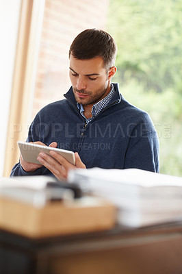 Buy stock photo Shot of a casual young man using a digital tablet at his desk